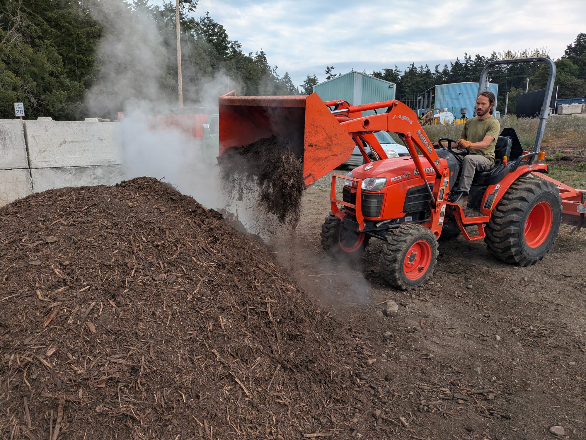 Keith Dixon working a compost pile in an orange tractor, with compost pile in the foreground.