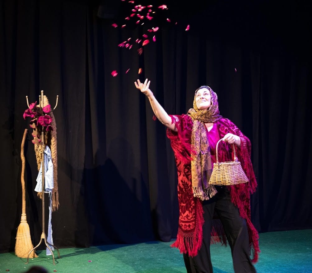 Zhaleh Almaee on stage in a red shawl and orange scarf tossing flower petals out of a basket.