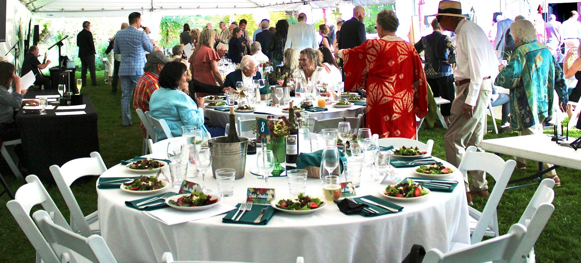A circular banquet table with white table cloth and chairs set with place settings and the salad course.