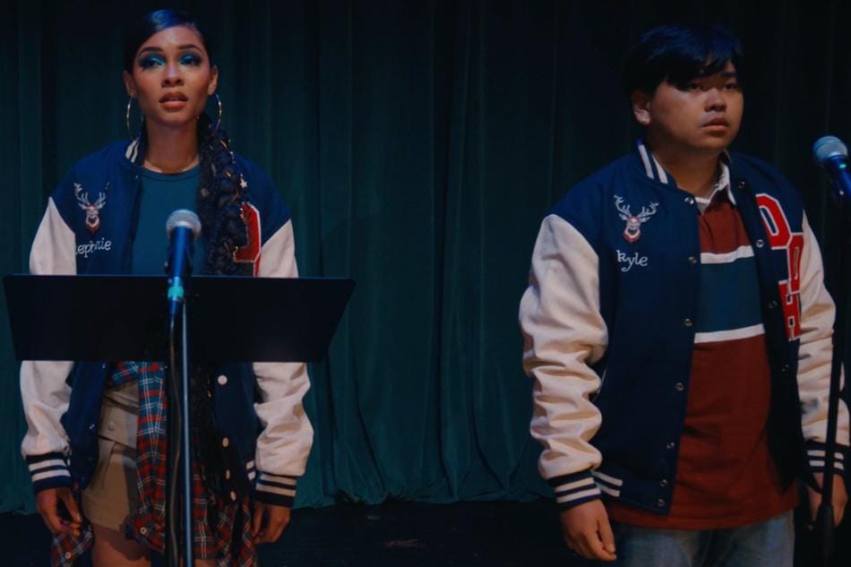 Two students in letter jackets on a stage in front of microphones. 