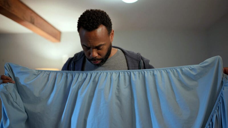 A man staring down at a blue fitted sheet. 