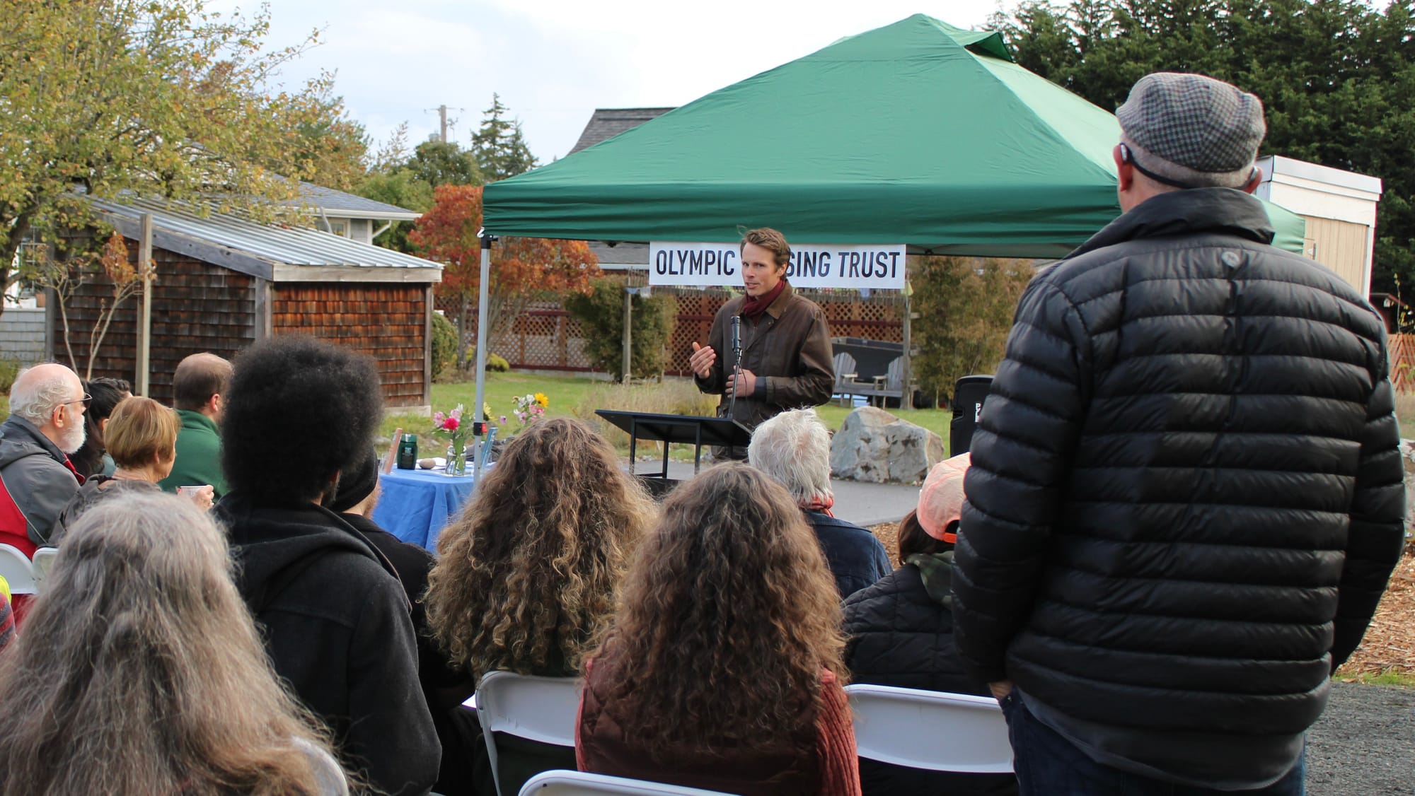 Kellen Lynch speaking before a crowd with a green tent in the background. 
