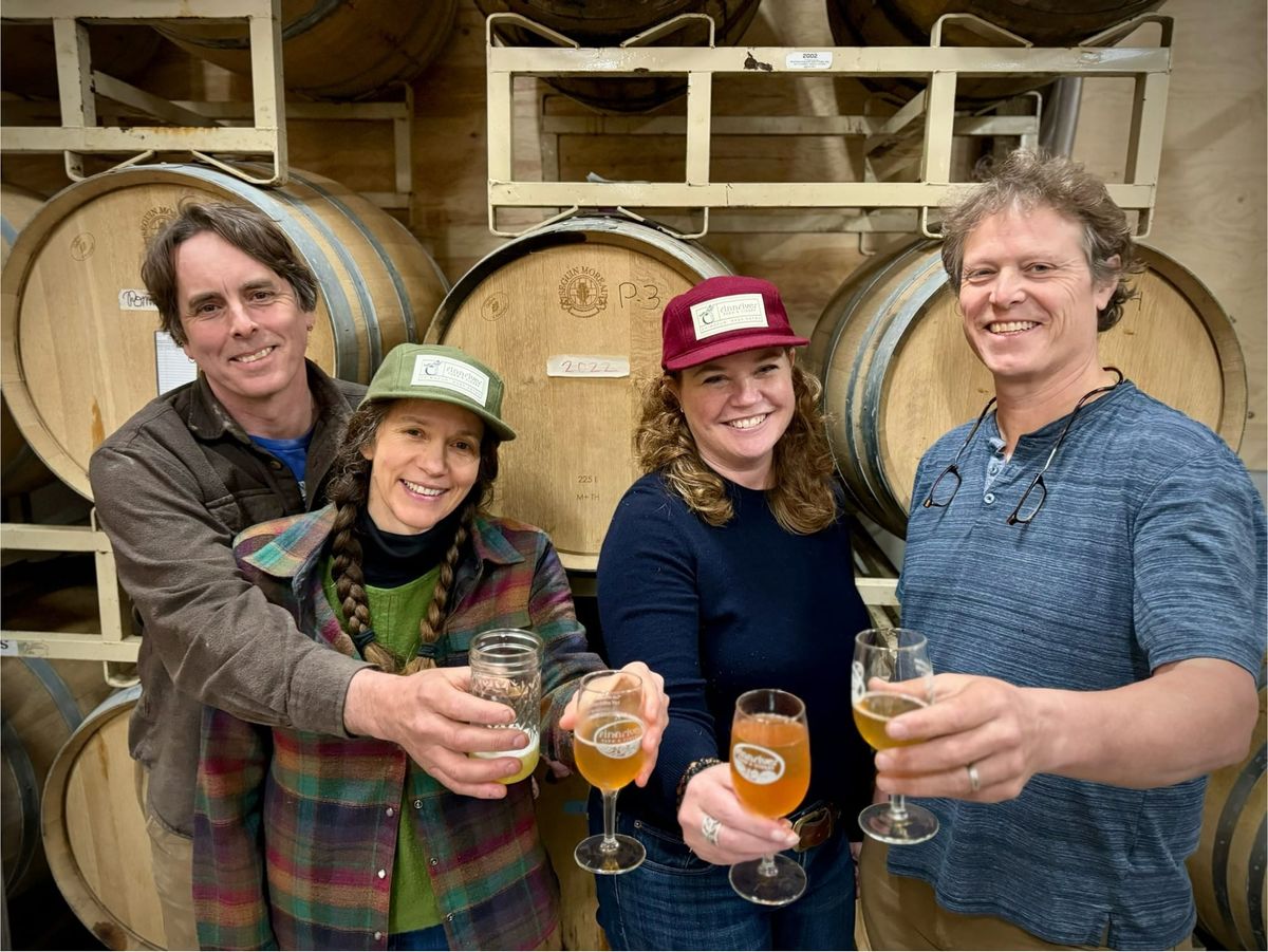 Founder/Owners holding out glasses of cider in front of casks of cider 