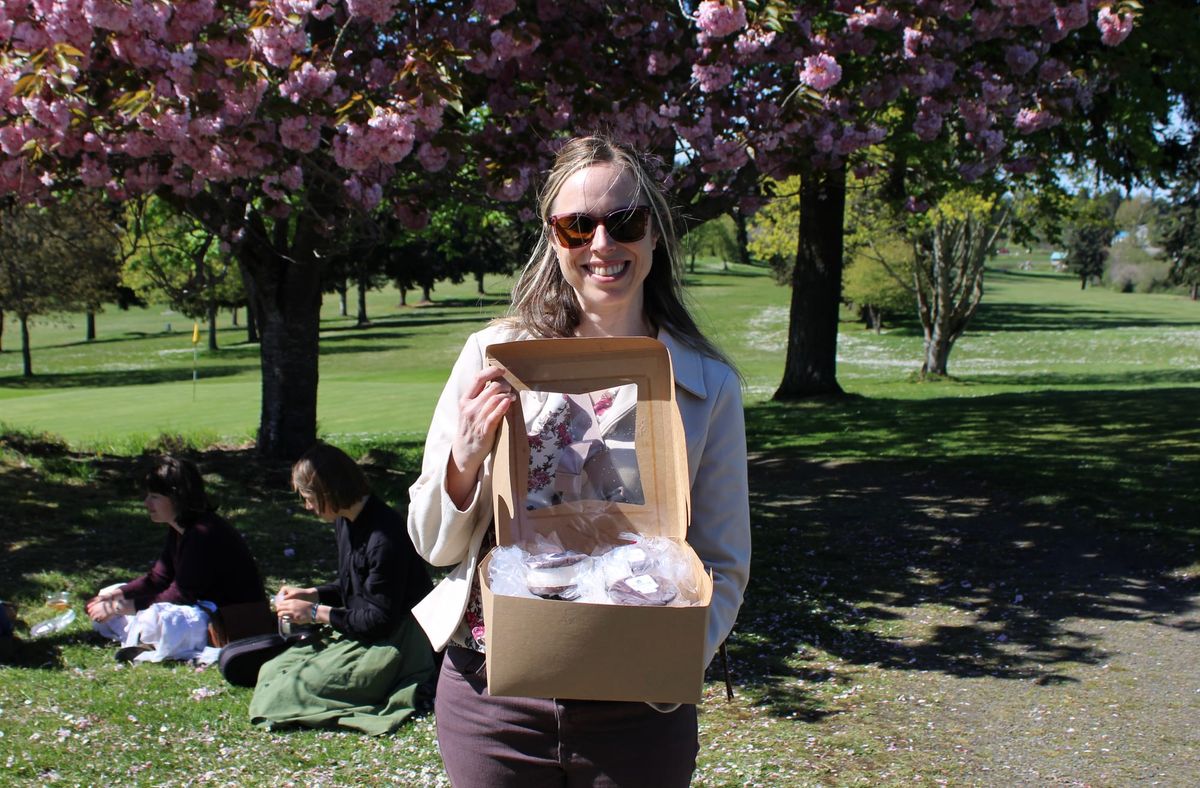 Emma Bolin passing out ice cream sandwiches in front of flowering trees. 