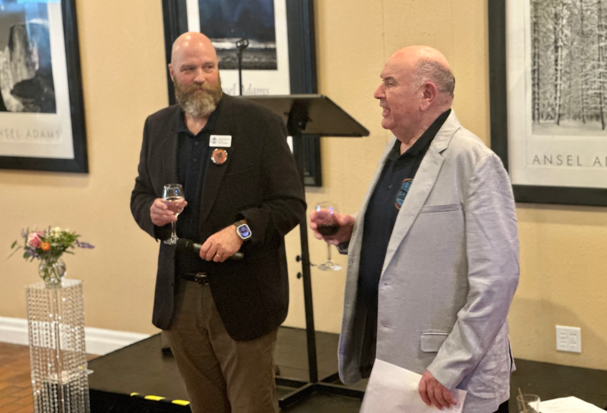 Mitch Brennan and Gary Keister with glasses in hand for a toast in front of a low stage
