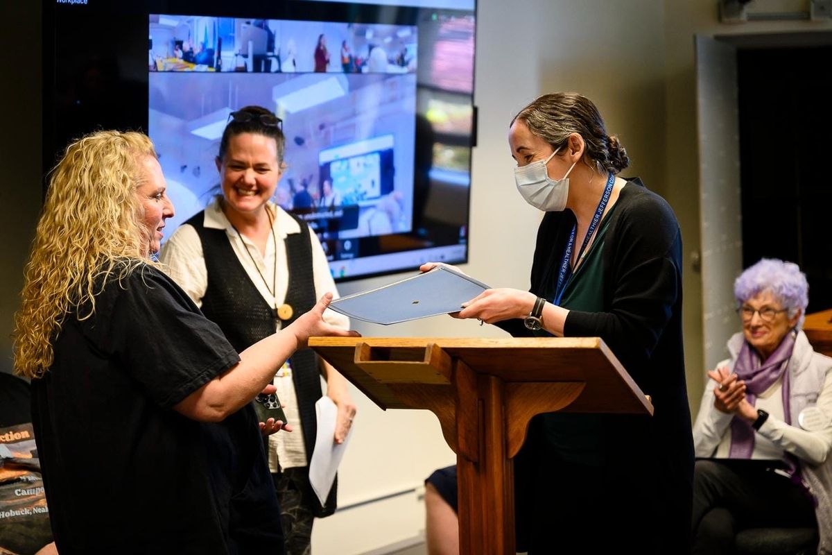 Stephanie Moran receiving Award to the left of a lectern as presenter and audience congratulate her. 