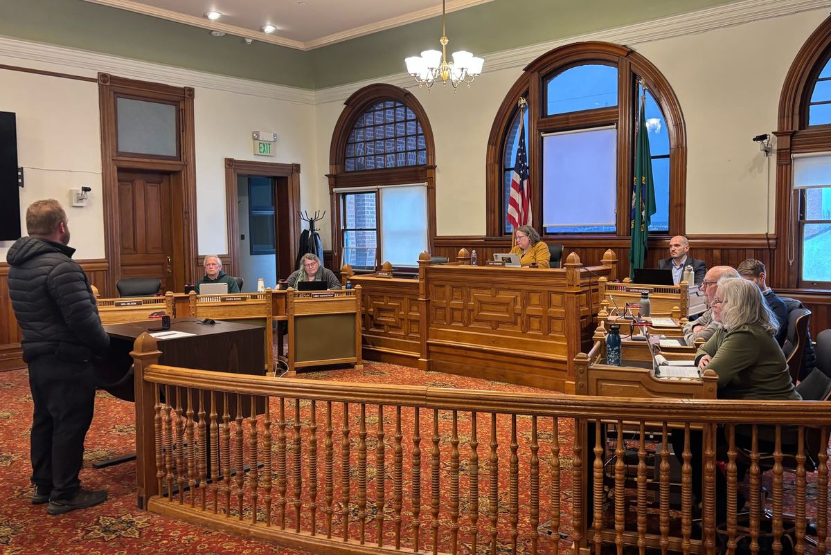 Ben Casserd in front of the city council bench next to a wooden banister on red patterned carpet