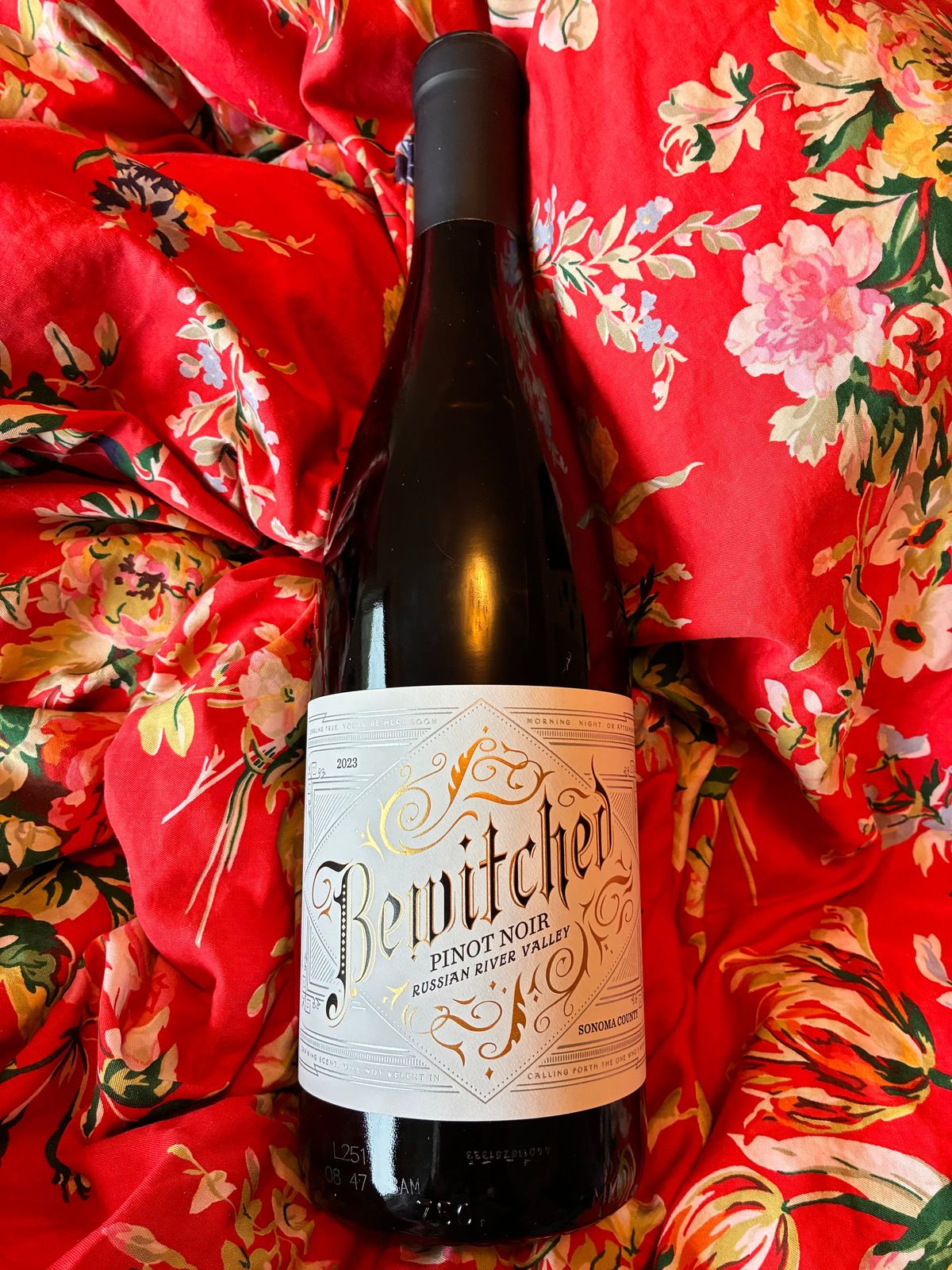 A bottle of Bewitched Pinot Noir in red flowered fabric 