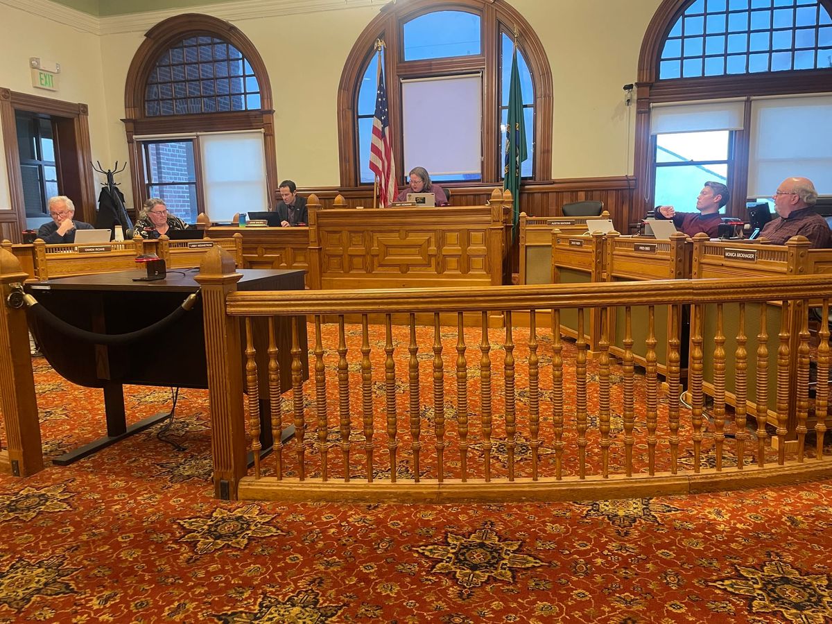 Council Members Business Meeting. A brown wooden banister in front of the mayor's bench and red patterned carpet.