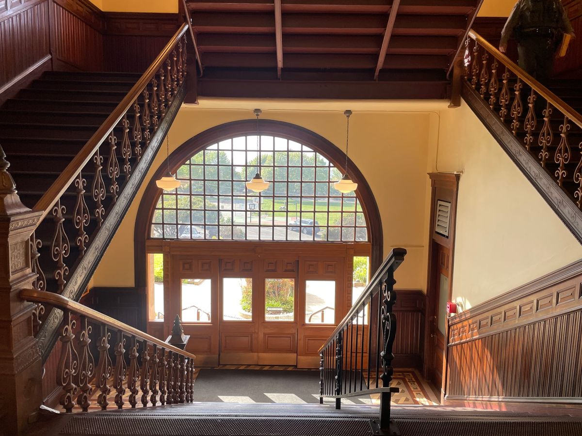 Looking down the courthouse staircase towards the "front" doors. Wood railing, wainscotting and doors.