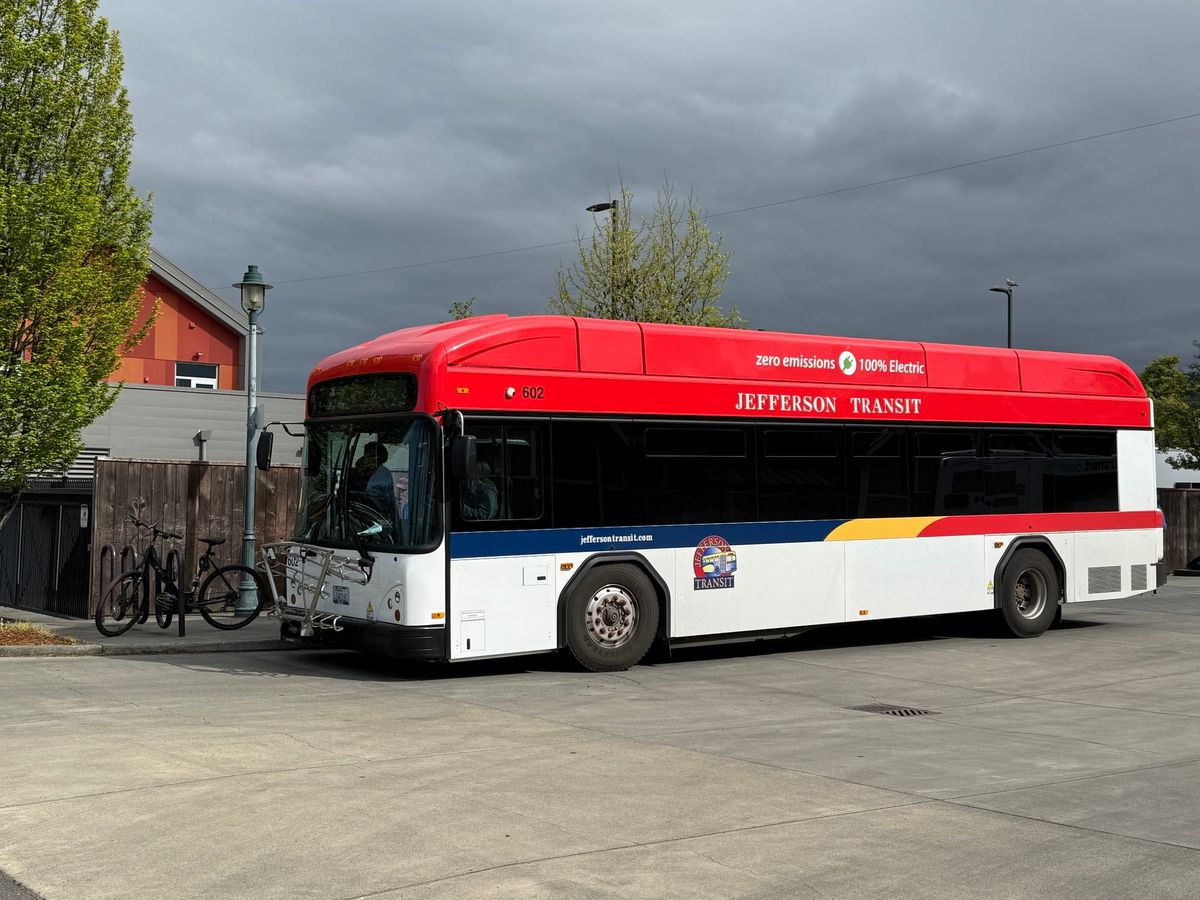 An electric bus with a red roof parked at a bus stop. 