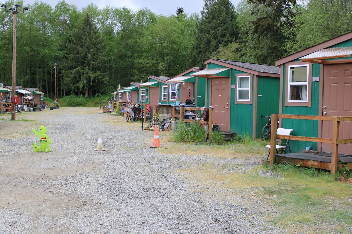 A row of tiny homes on a gravel driveway. Green painted cabins with brown doors and brown trim. 
