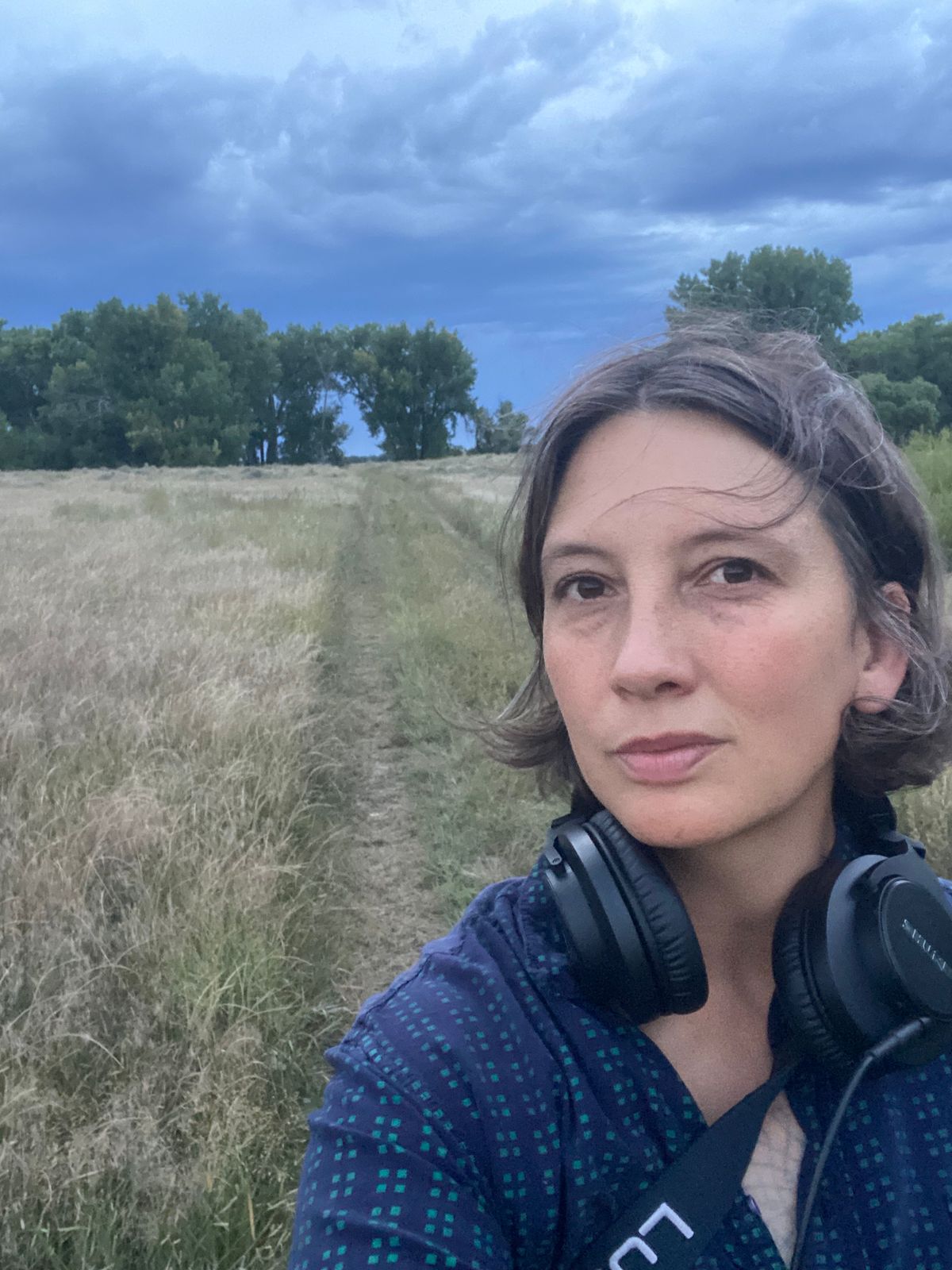 Nhatt Nichols with headphones in front of a prairie with some trees. 