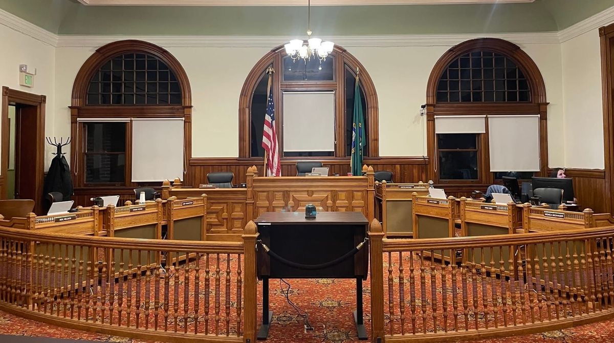 A three desk bench, with three desks on each side and a banister barrier with guest lectern in the middle. 
