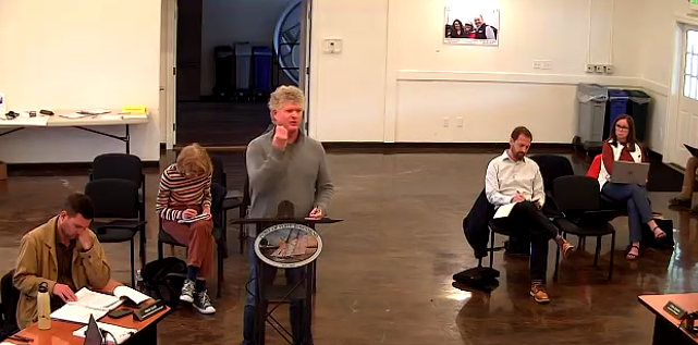 Jeff Randall speaking at a lectern with a seated audience behind him taking notes and listening.