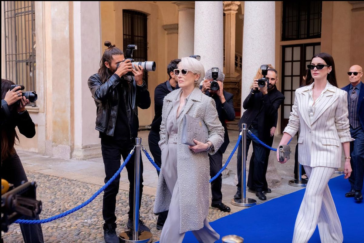 Meryl Streep and Anne Hathaway walk down a blue carpet with photographers in the background. 
