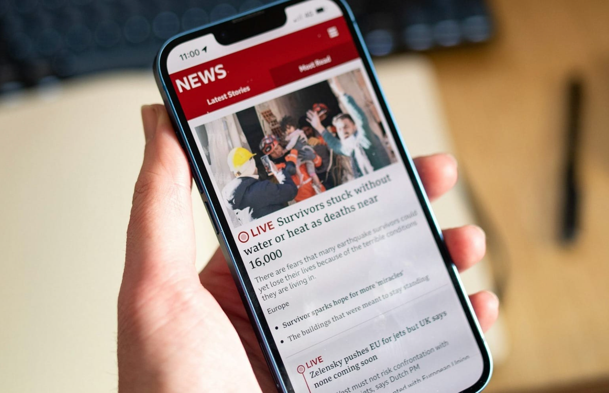 Image of user holding a phone in their hand, and the screen shows miscellaneous news headlines.