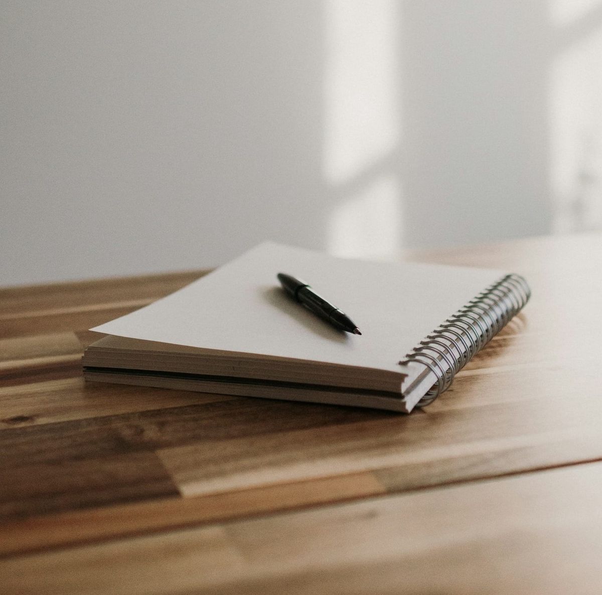 A notebook on a wooden table with a pen resting on top of it. 