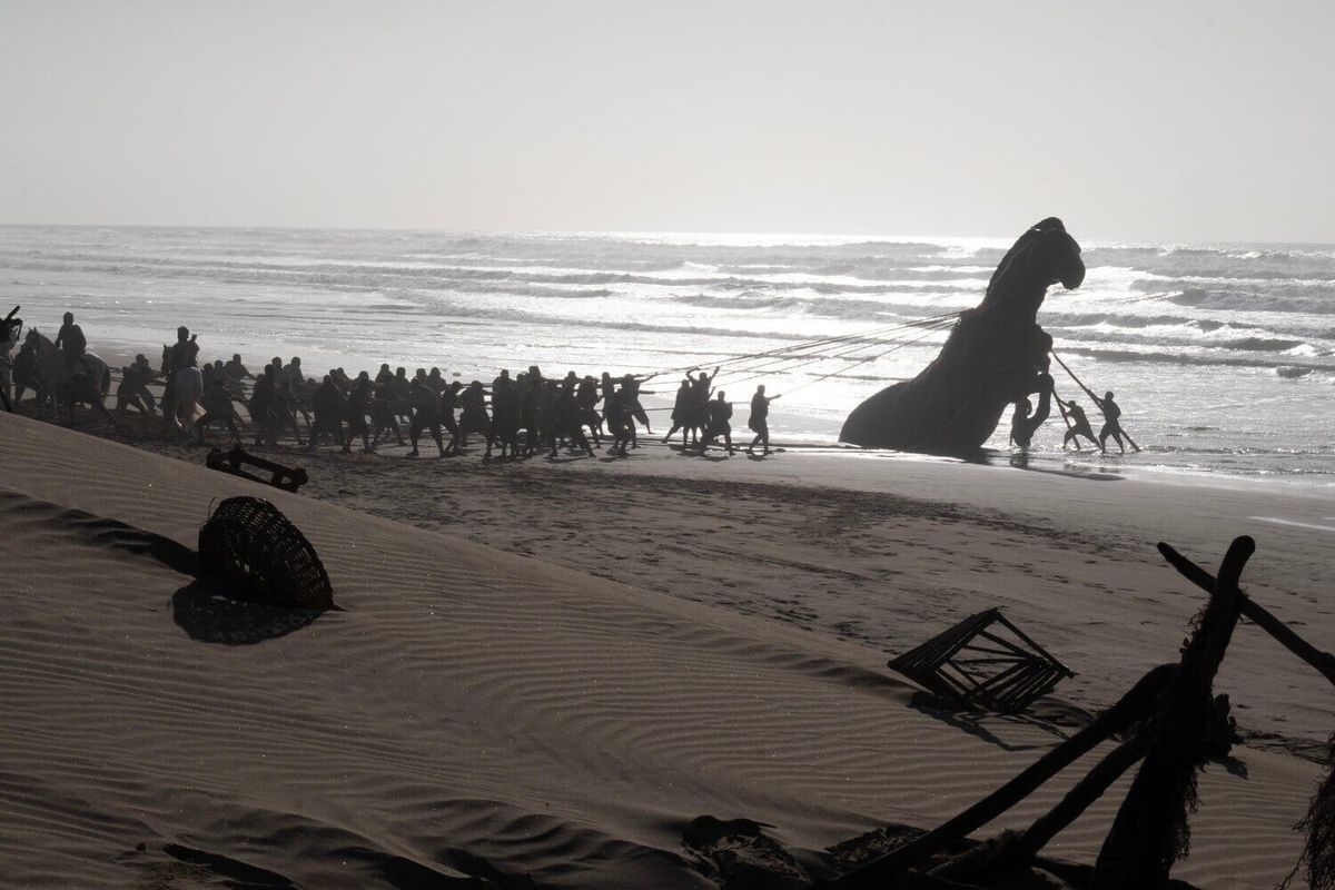 The Trojan Horse with soldiers on the beach with the horse tethered by the soldiers and in the water.