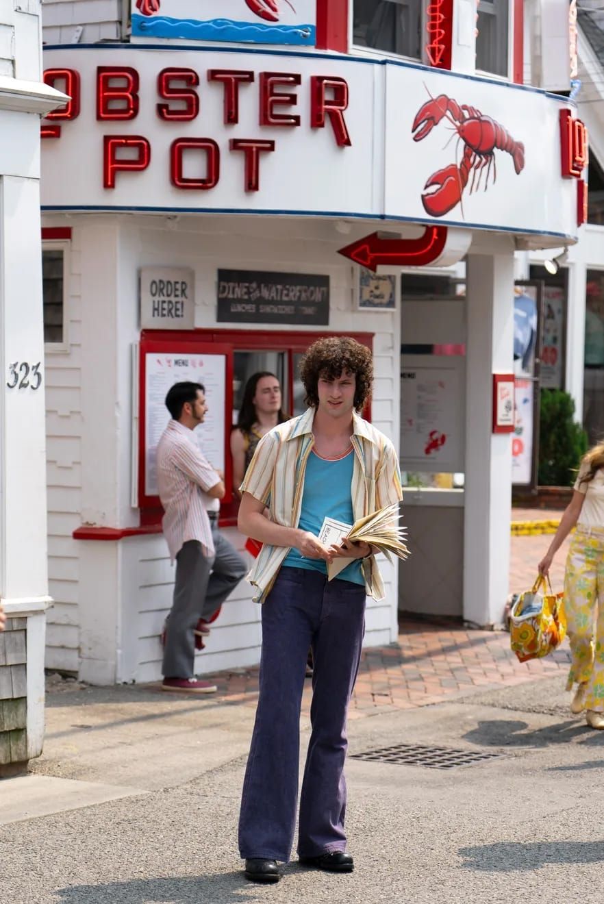 Dominic Sessa as Anthony Bourdain standing in front of a restaurant called "Lobster Pot".