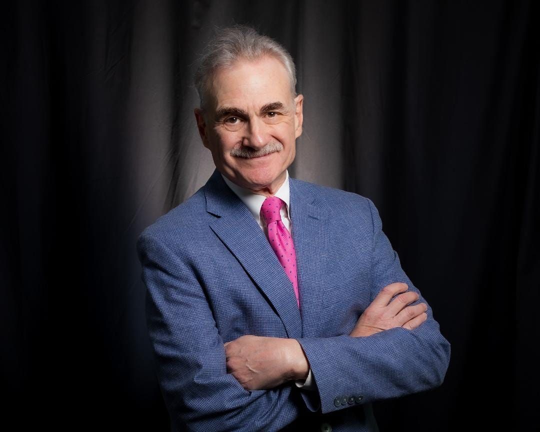 Murray Horwitz in a blue suit with a pink tie. 