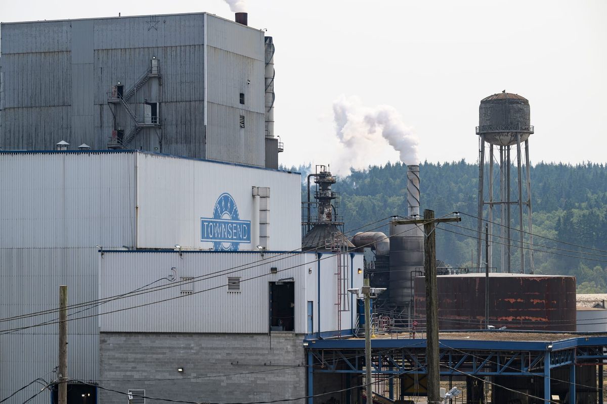 The Port Townsend Paper Company, a gray metal building with a smoke stack and a water tower to the right. 