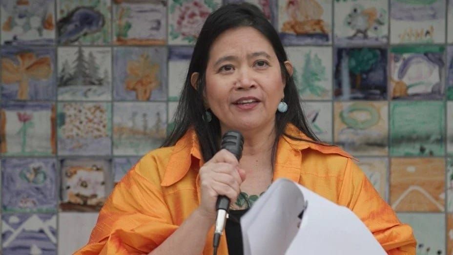 Port Townsend city Poet Laureate Rufina C. Garay in an orange shirt talking into a microphone. 