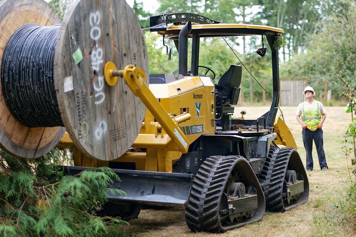 A yellow vibrating plow on four continuous track treads, with a fiber optic spool elevated in the front. 