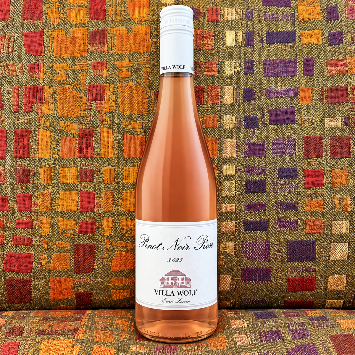 A clear bottle of Villa Wolf 2025 Pinot Noir Rosé in front of a colorfully patterned fabric background. 