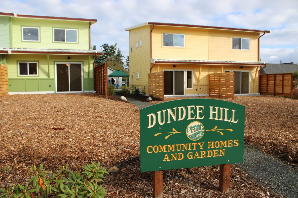 Street view of the Dundee Hill development, a green duplex to the left and a yellow duplex to the right with a path down the middle and sign in the foreground. 