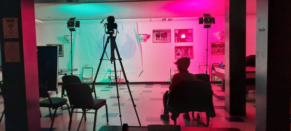 A room with fuchsia lighting, chairs and one person sitting in a chair in the foreground on the right 
