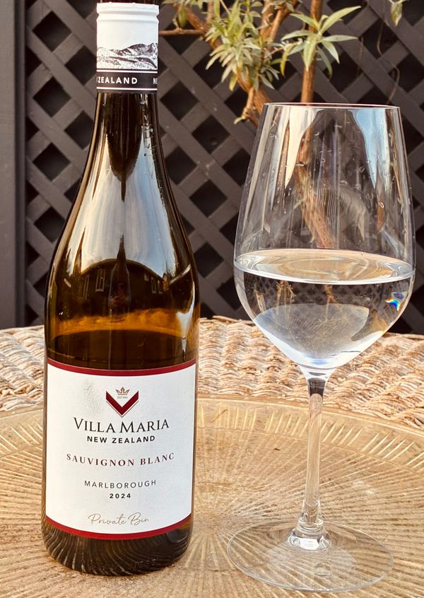 A bottle of white wine in a brown bottle with a glass of the wine to the right 