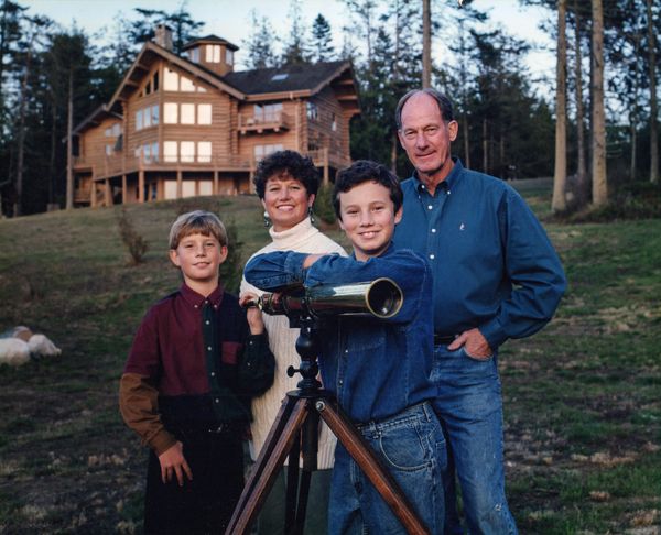 The family in front of their log cabin home posing with a telescope. 