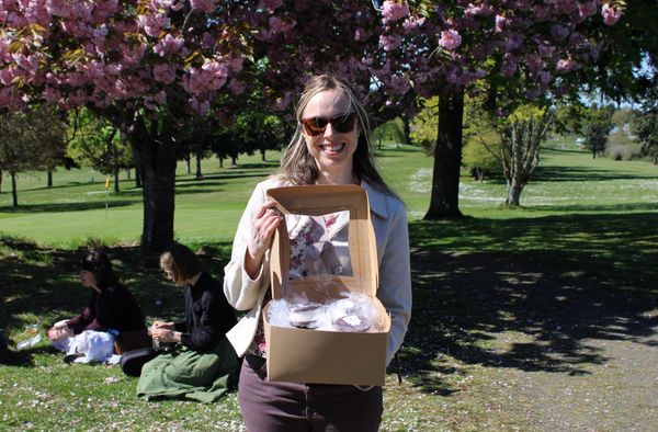 Emma Bolin passing out ice cream sandwiches in front of flowering trees. 