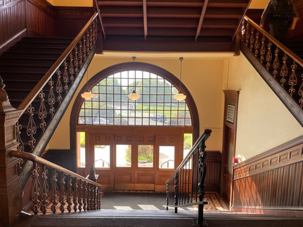 Looking down the courthouse staircase towards the "front" doors. Wood railing, wainscotting and doors.