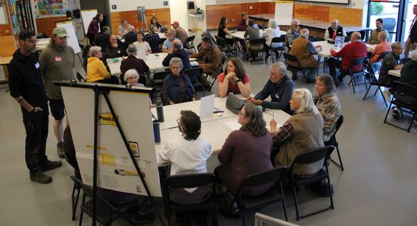 Port Townsend residents sitting at round tables fronted by a large easel wiht a pad of paper. 