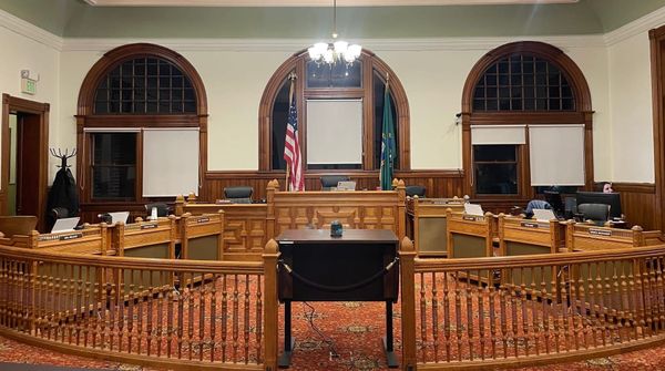 A three desk bench, with three desks on each side and a banister barrier with guest lectern in the middle. 