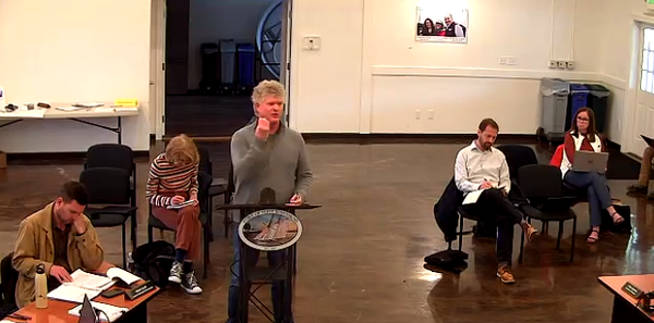 Jeff Randall speaking at a lectern with a seated audience behind him taking notes and listening.