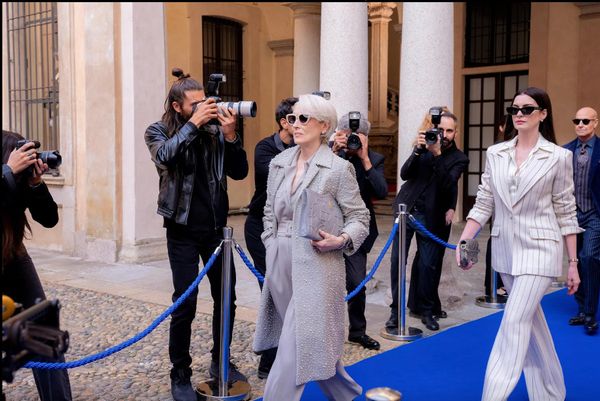 Meryl Streep and Anne Hathaway walk down a blue carpet with photographers in the background. 