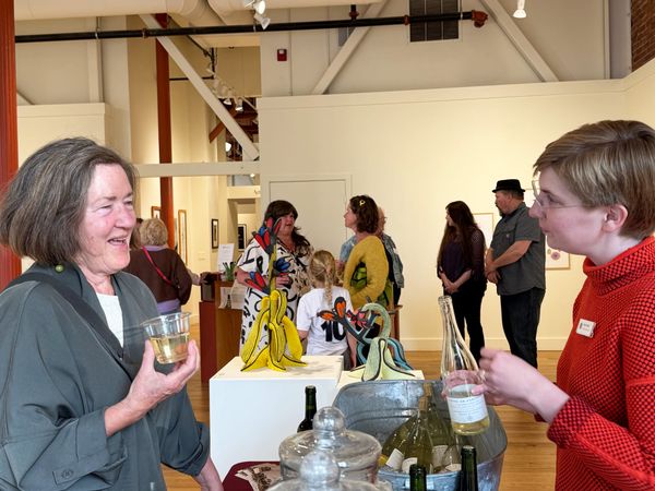 Linda Dowdell, left, talks and imbibes with Anna Teiche in the gallery, with art lovers in the background.