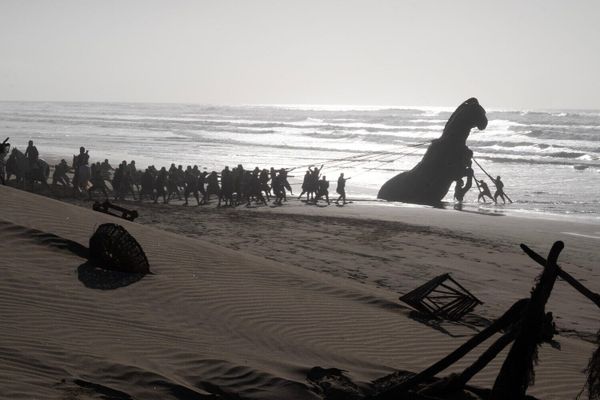 The Trojan Horse with soldiers on the beach with the horse tethered by the soldiers and in the water.