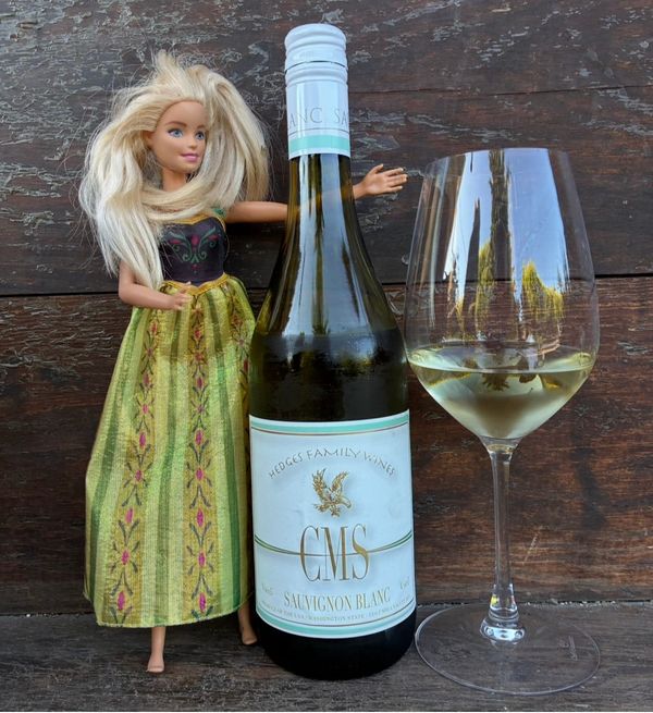 Barbie at left with a bottle of CMS Sauvignon Blanc at center and a poured glass of white wine to the right.