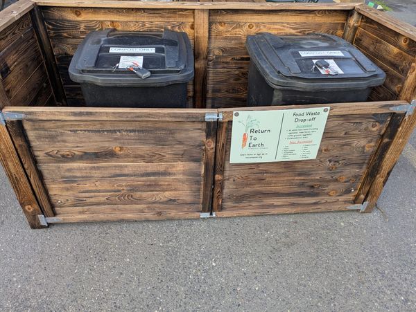 Two padlocked food waste bins in a gated wooden corral. 