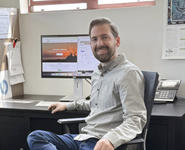 David Ballif smiling for the photo at his desk in front of his computer. 