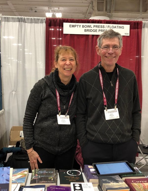 Holly J. Hughes and John Pierce in front of Empty Bowl Press published books at the Association of Writers & Writing Programs book fair in Seattle in 2023.