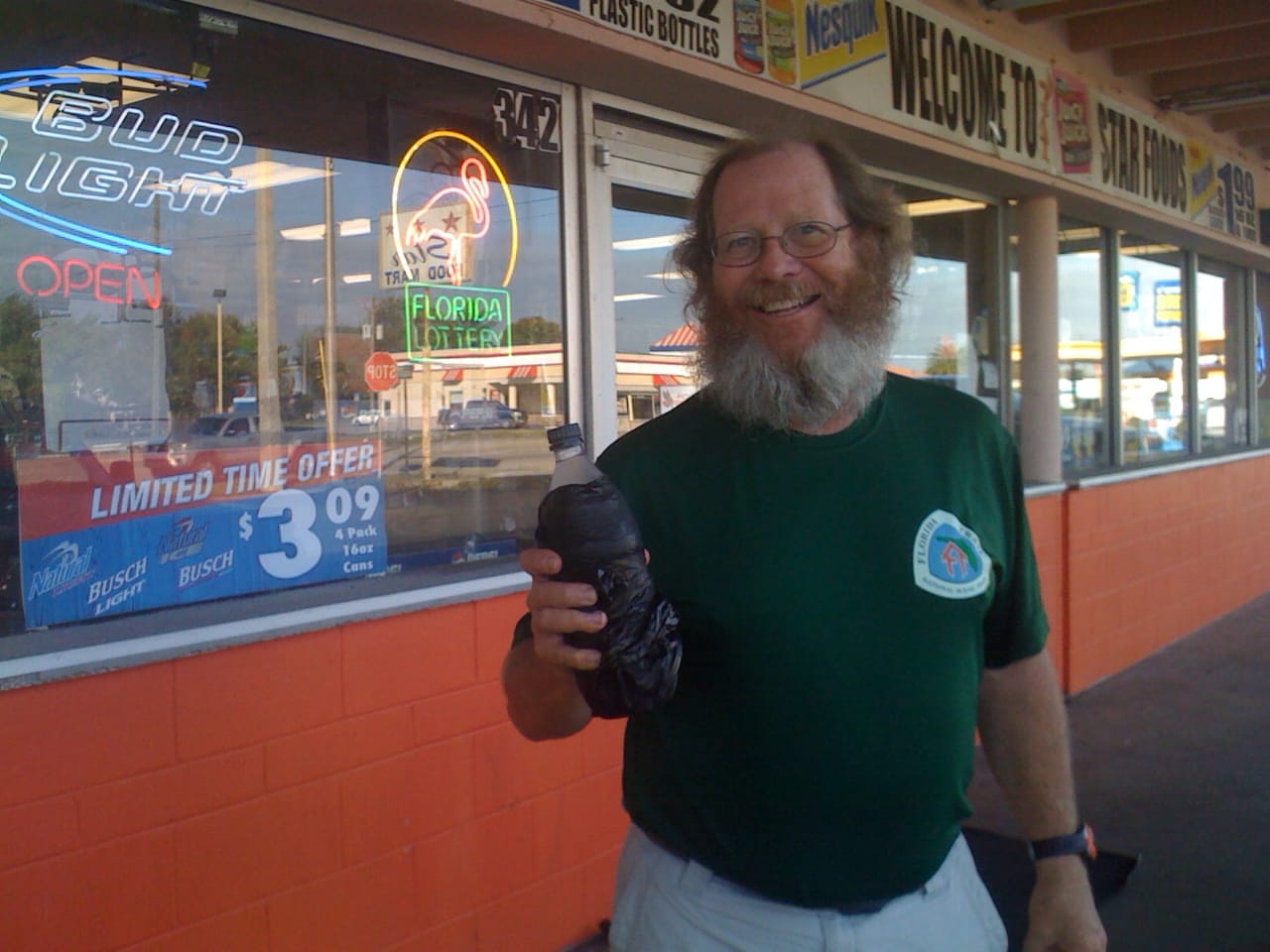 Man with a Florida Trail shirt and crazy beard and red hair holding an unmarked bottle outside of a convenience store