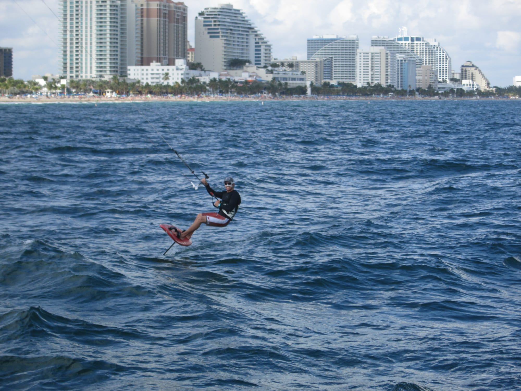 Man on a sailboard hovering over the waves with a city skyline beach background