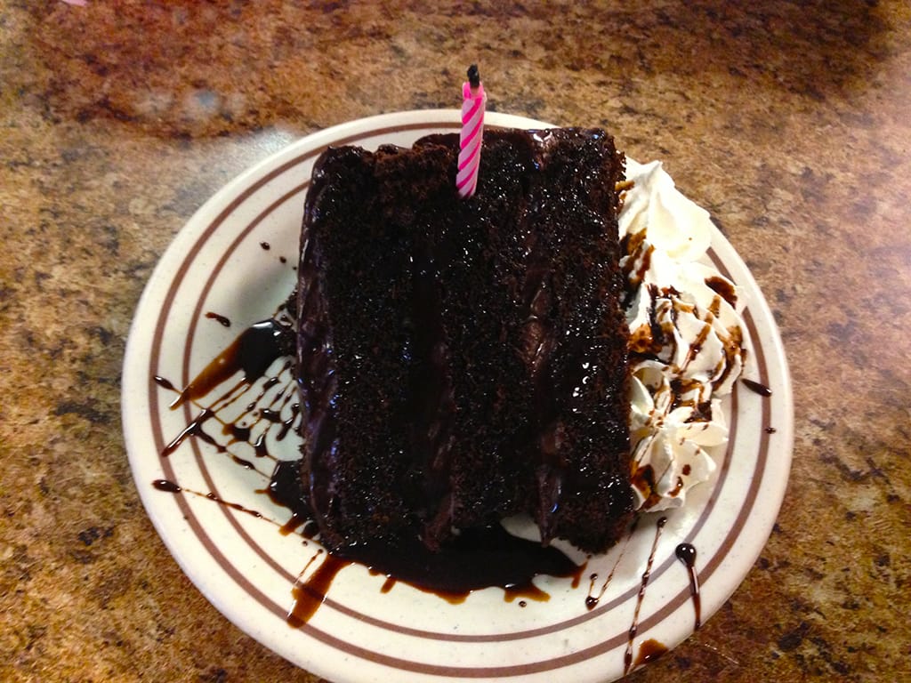 Chocolate cake on a plate with drizzle and a candle