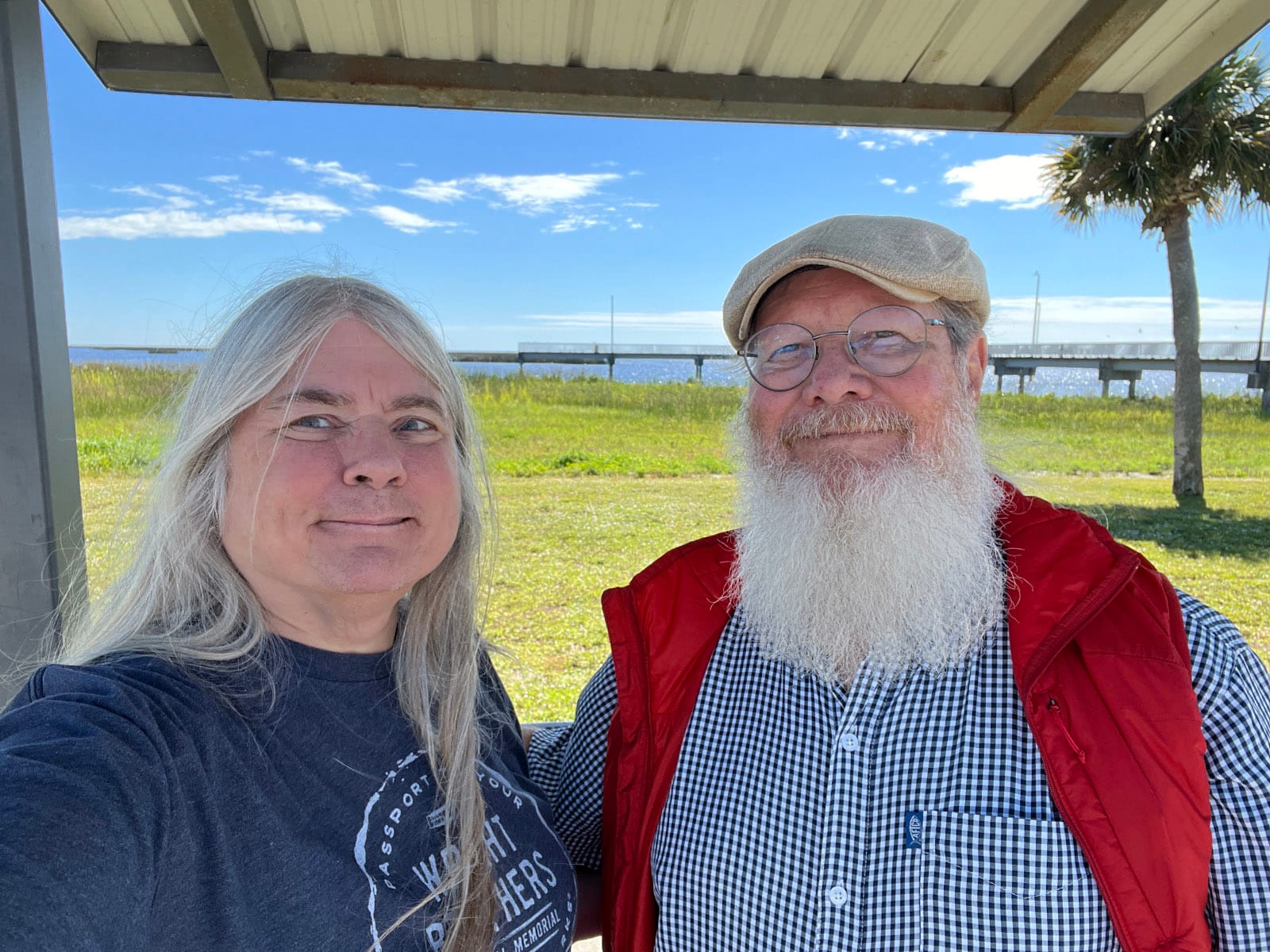Woman and man under picnic shelter roof with lake and pier in background