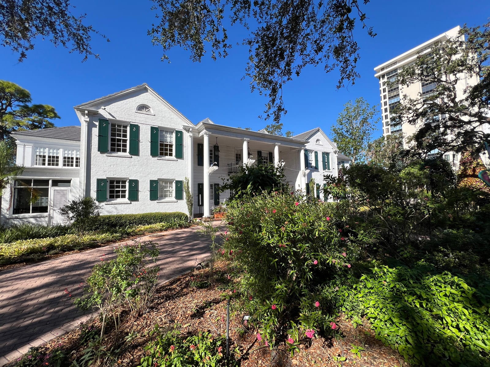 White mansion with green shutters with gardens in front